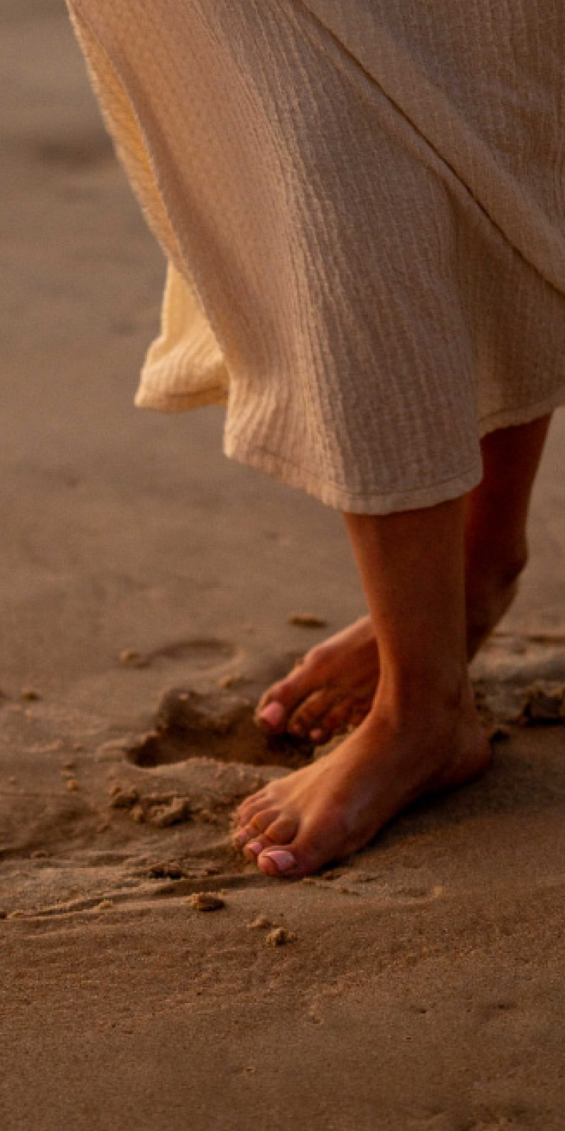 Bare feet walking across wet sand at sunset