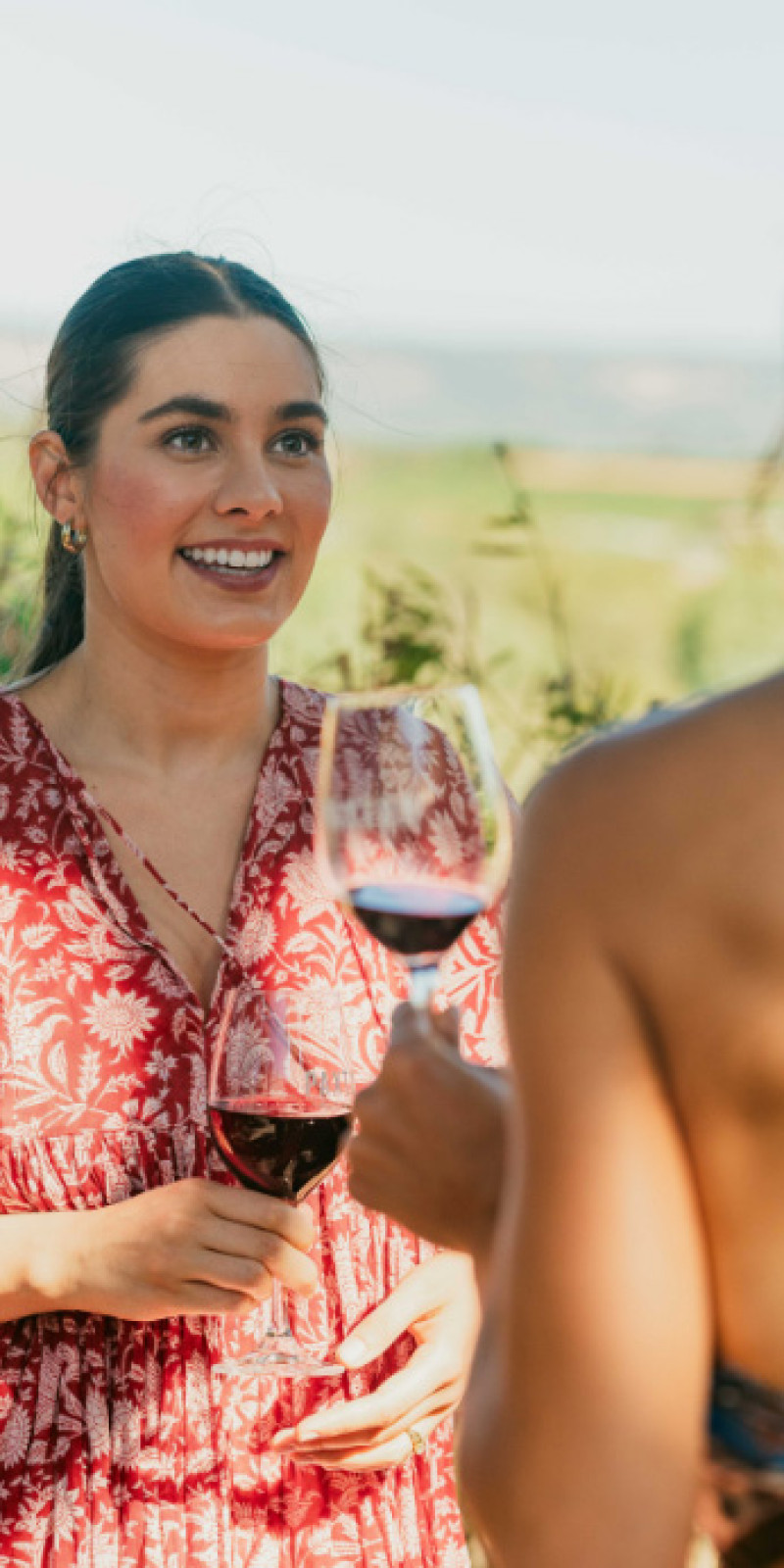 Two women holding glasses of red wine outdoors at golden hour