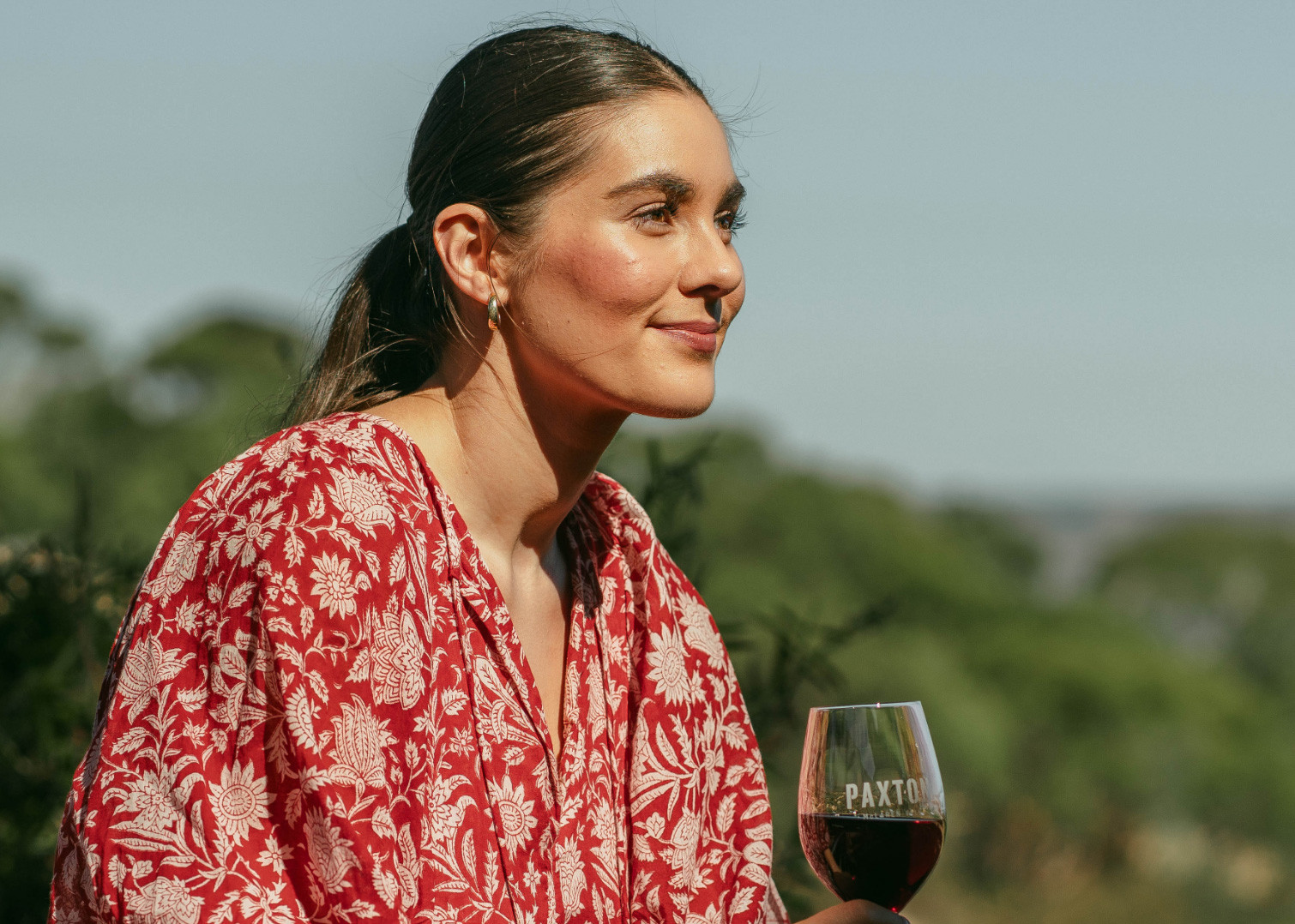 A woman holding a glass of red wine in a vineyard