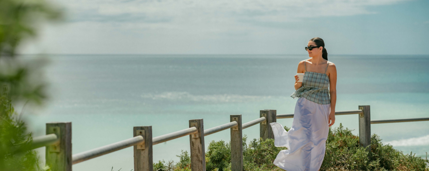 A woman walking along a coastal boardwalk above the beach