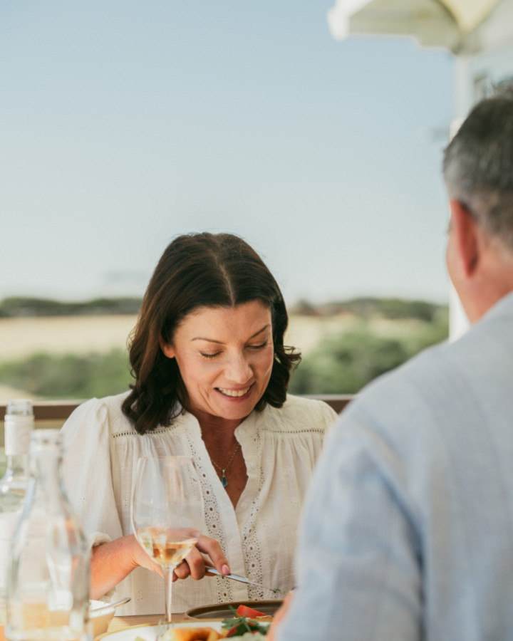 A woman eating a meal at an outdoor table with a glass of white wine