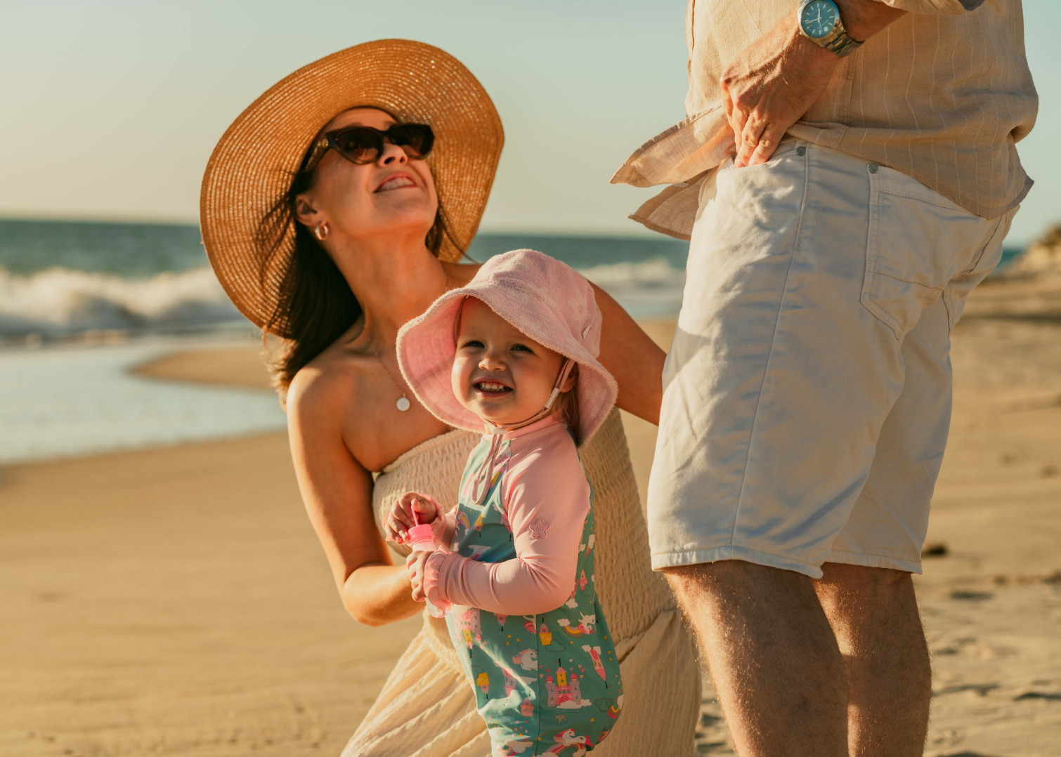 A woman in a sun hat holding a toddler on the beach